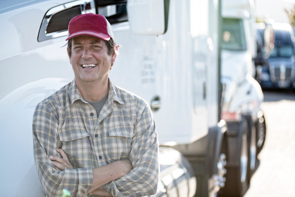 Caucasian man truck driver with his truck parked in a lot at a truck stop.